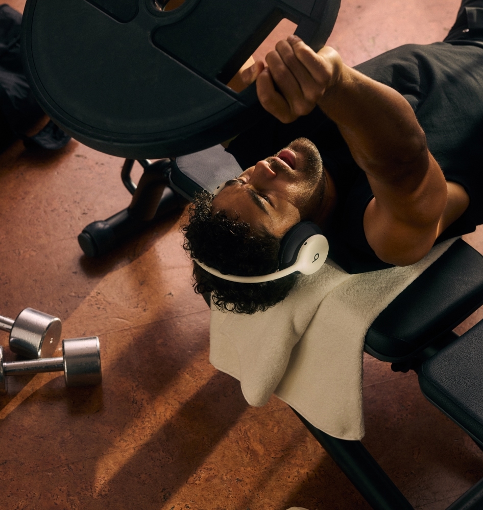 A man lifting weights on a bench while wearing Beats 360 headphones during a workout