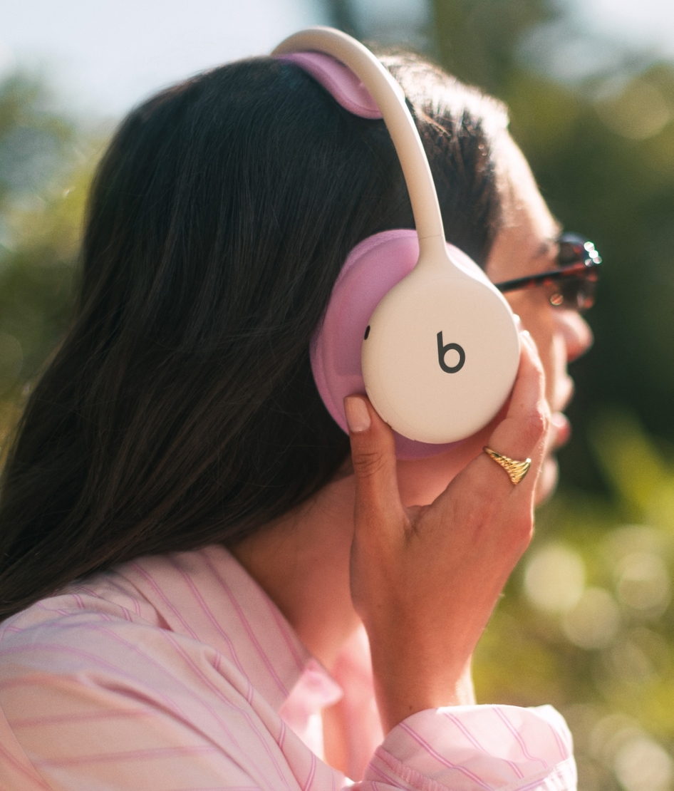 A woman outdoors wearing Beats 360 headphones with pink ear cushions, adjusting the fit against her ear