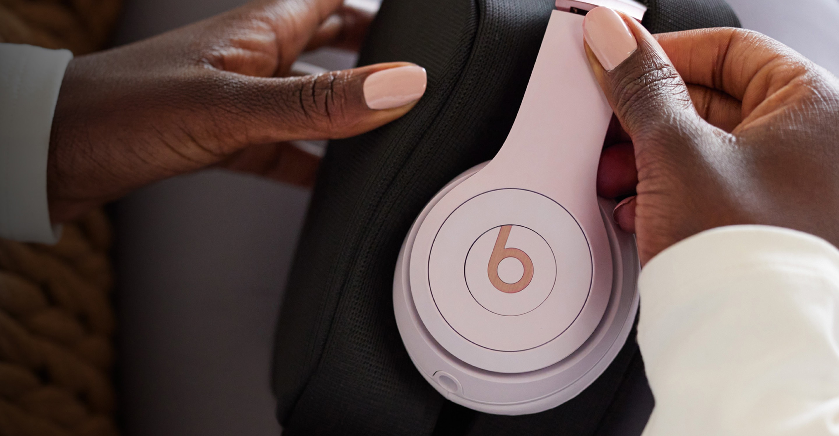 A woman's hands placing Cloud Pink Beats Solo 4 headphones into a black carrying case
