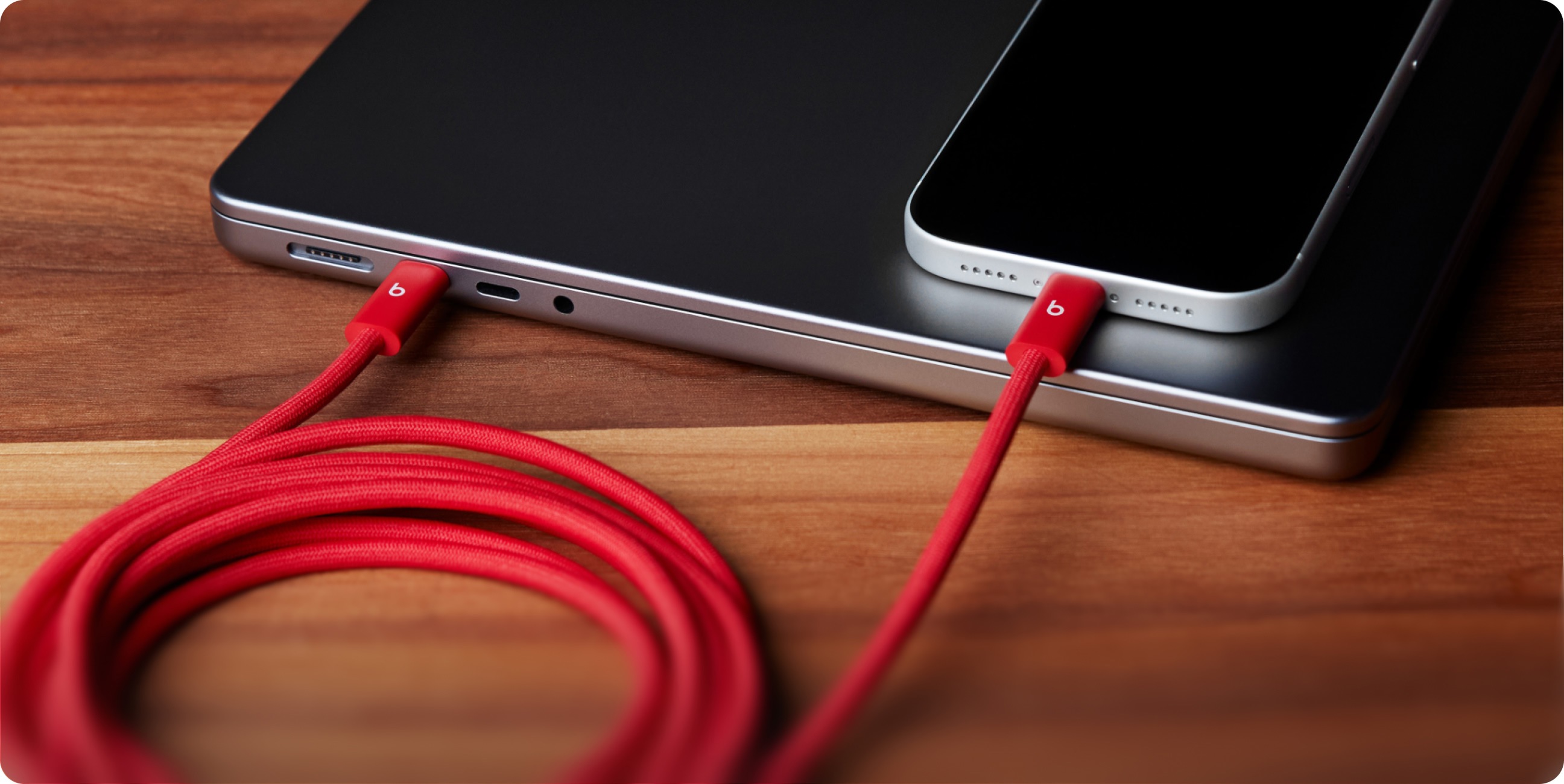 A coiled Beats 240W USB-C to USB-C Cable plugged into electronic devices to demonstrate fast charging.