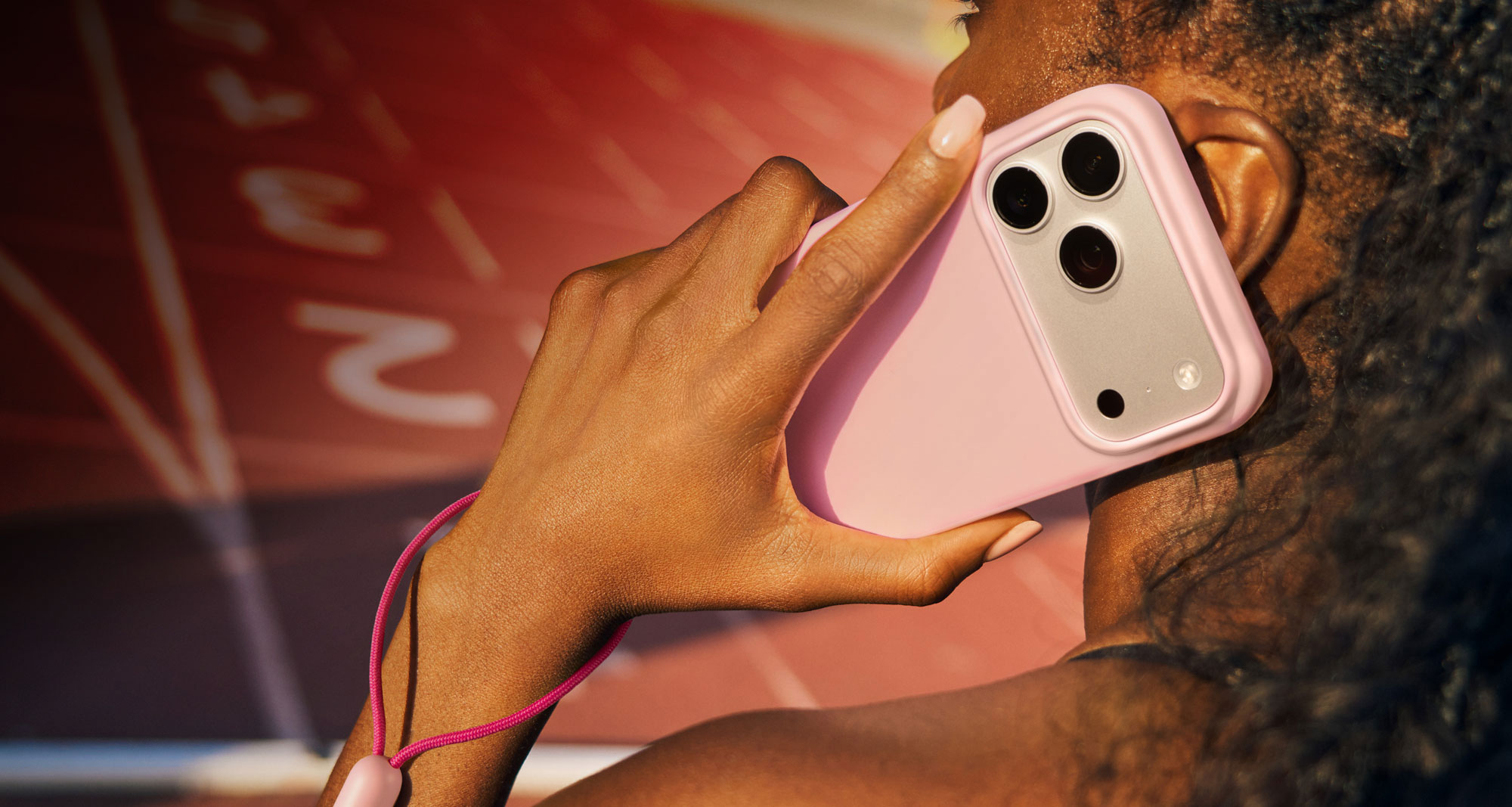 A woman talking on the phone holding the Beats iPhone 17 Kickstand Case with MagSafe and Camera Control in Pebble Pink showcasing the removable lanyard.
