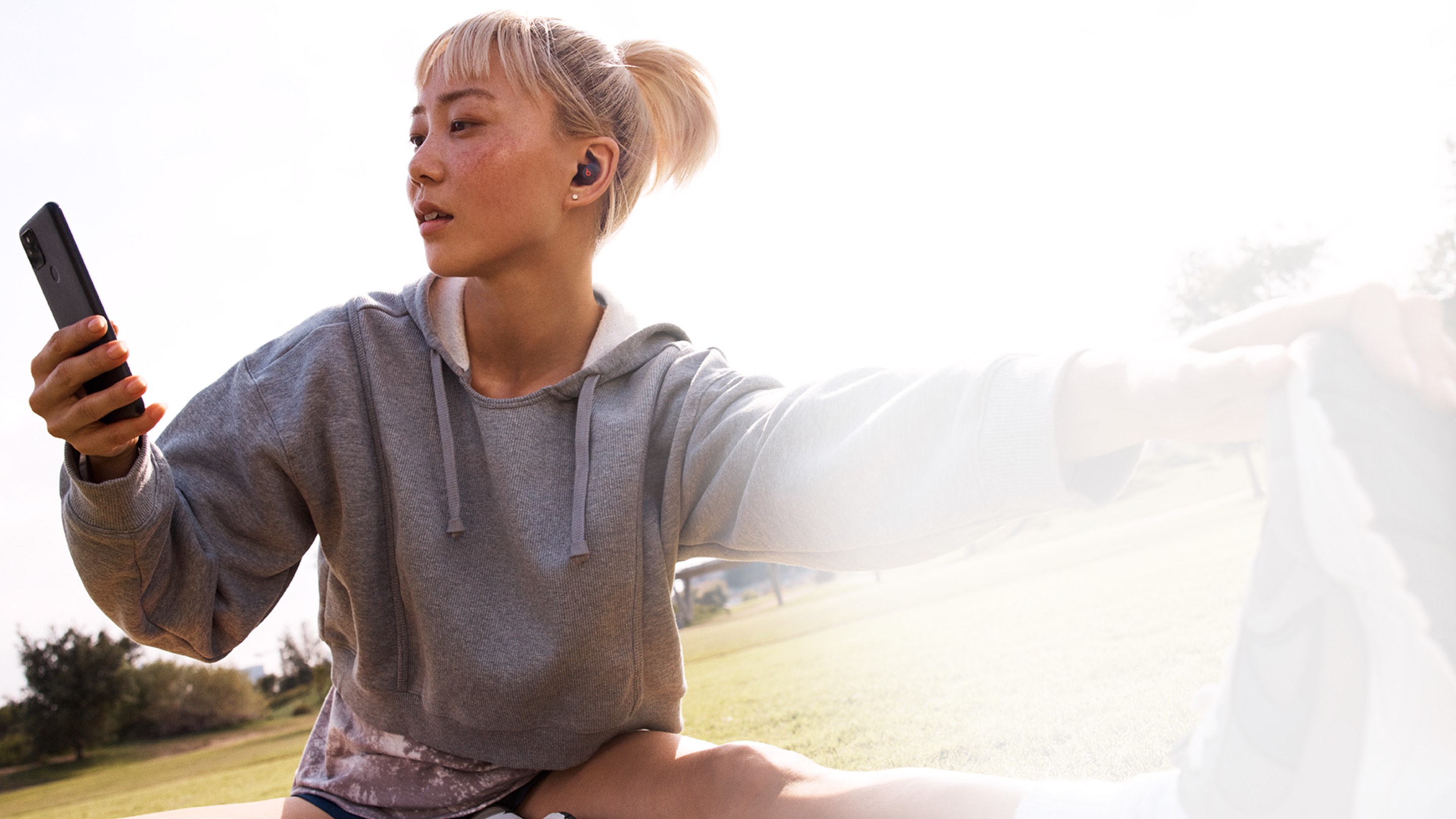 Woman wearing beats fit pro and accessing her Android device while stretching outdoors