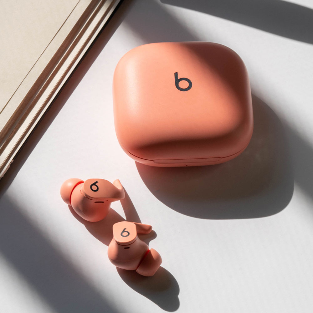 Beats Fit Pro earbuds and matching charging case in Coral Pink on a table. 