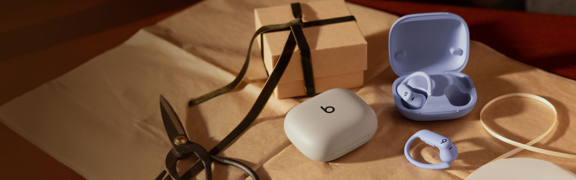 Powerbeats Pro 2 in Quick Sand and Hyper Purple, scissors, and a gift on top of wrapping paper.