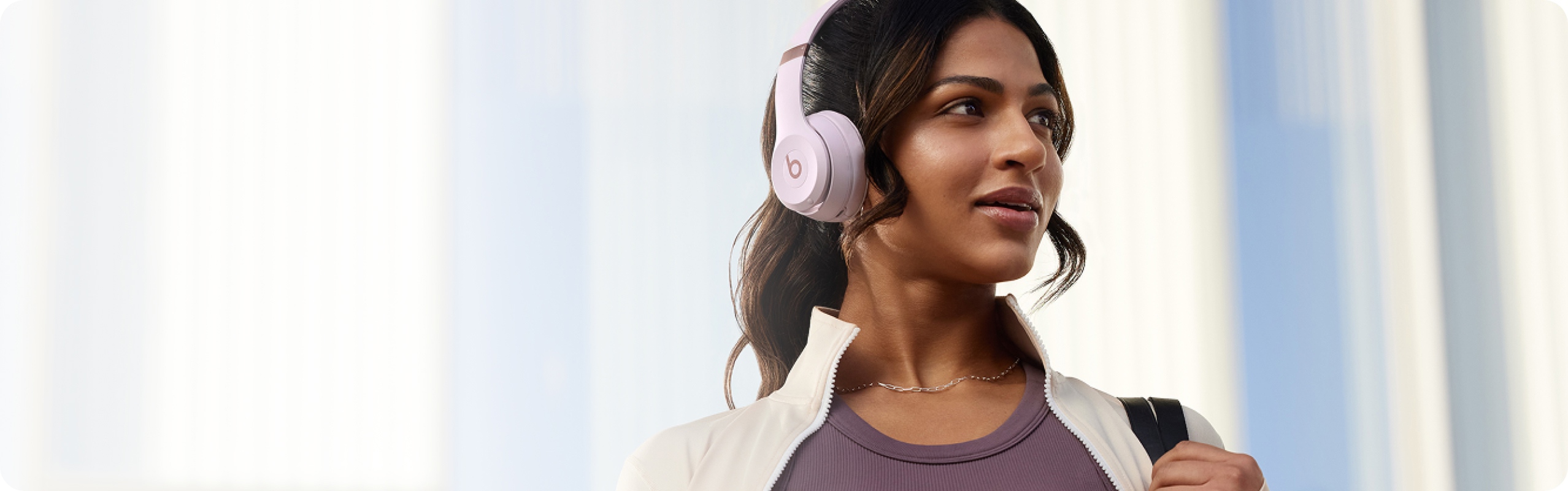 Woman wearing Cloud Pink Beats Solo 4 headphones against a soft blue backdrop