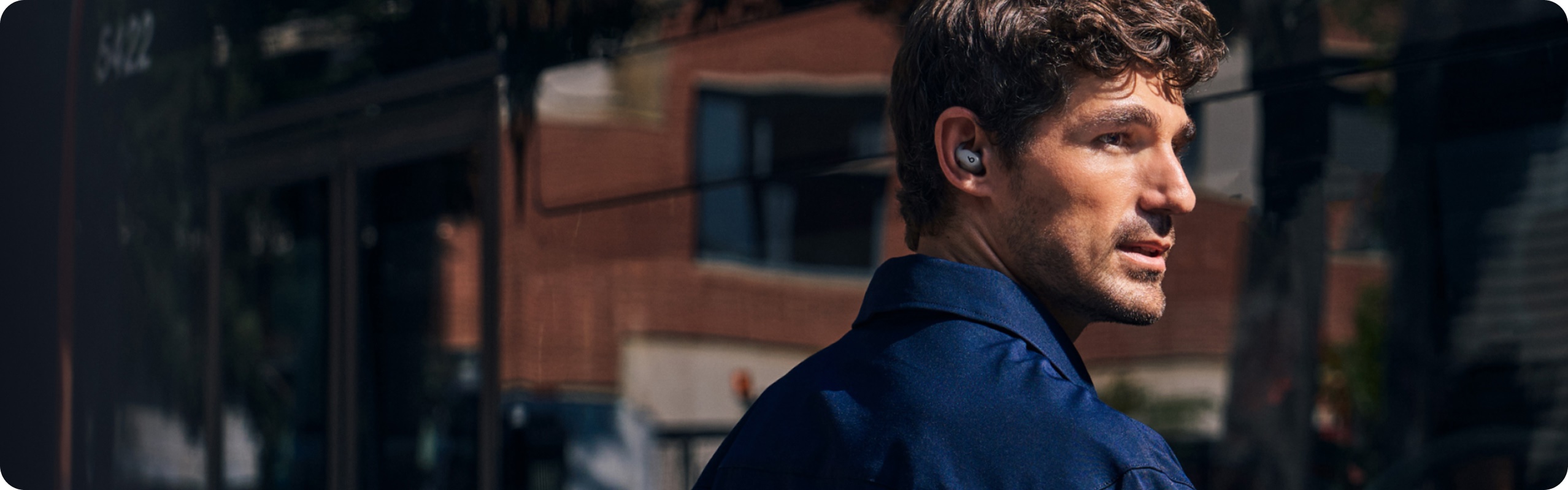 Man wearing Gravel Gray Powerbeats Fit earbuds on a sunny city street